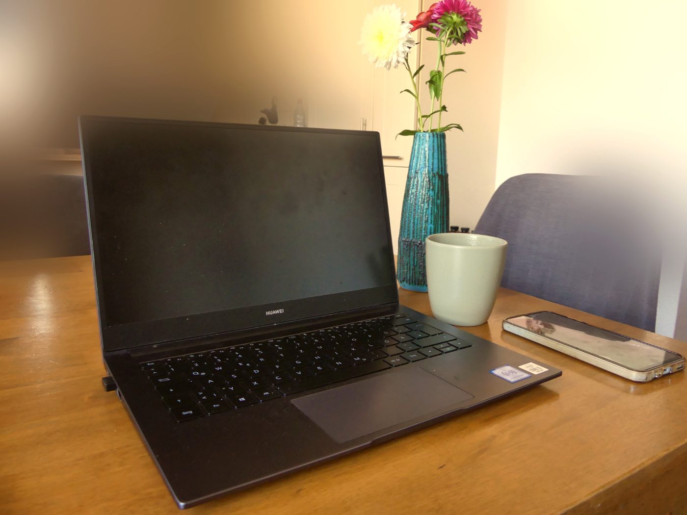 Mutter mit Kind auf dem Arm, beide lachen, warmes Tageslicht, Homeoffice-Atmosphäre im Hintergrund, Bücherregal und Pflanze sichtbar, Terrakotta-Töne