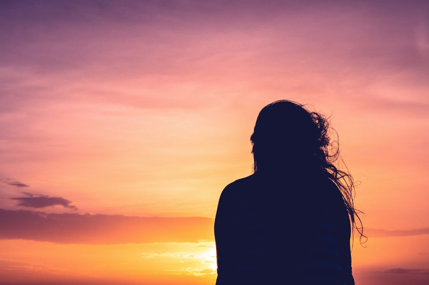 Silhouette einer Frau vor warmem Sonnenuntergangshimmel, Symbolbild für einen neuen Anfang