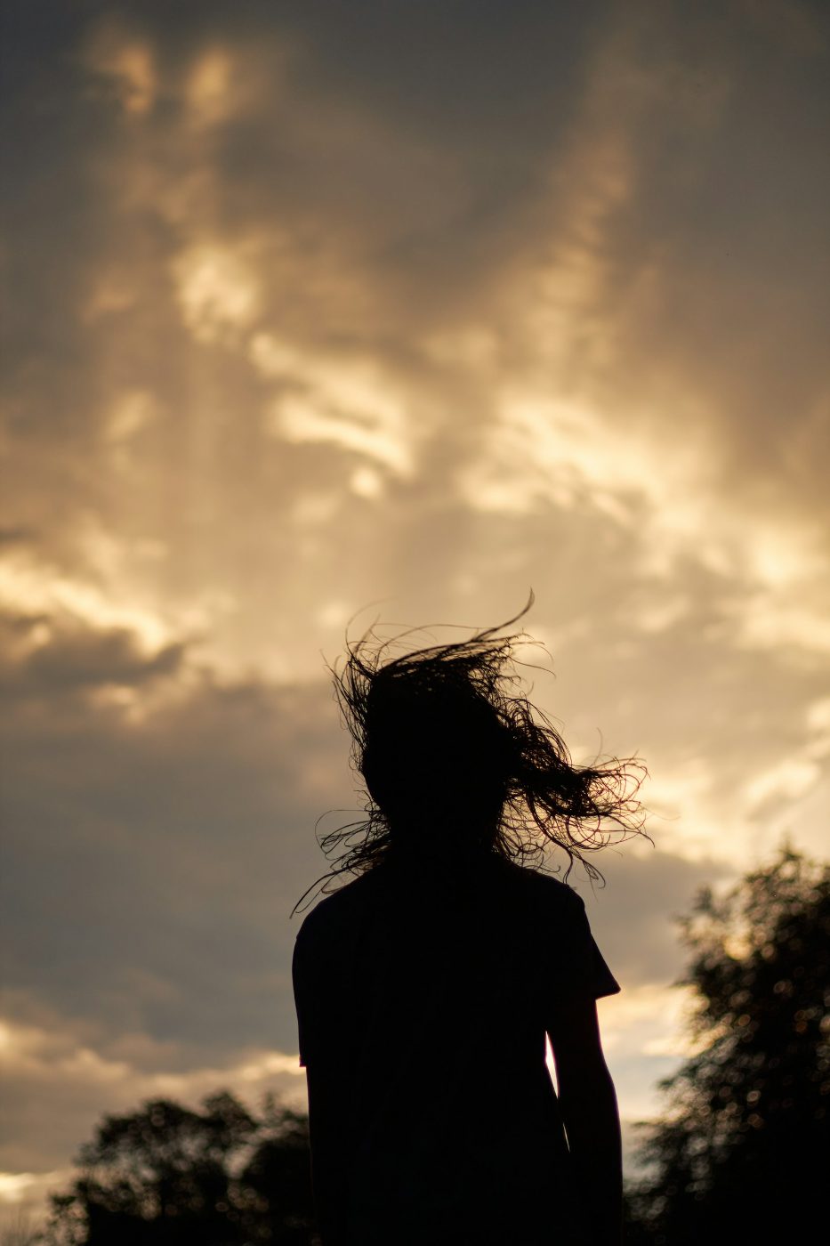 Silhouette einer Frau von hinten mit windbewegtem Haar vor warmem Sonnenuntergangshimmel
