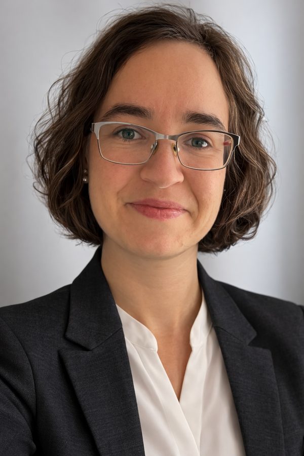 Carolin, 32, lächelt offen in die Kamera, Halbporträt in warmem Tageslicht, natürlicher Hintergrund in sanften Erdtönen, entspannte Alltagsatmosphäre